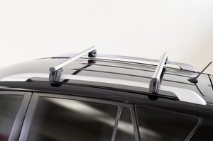 two grey roof bars mounted on two original longitudinal bars of a dark vehicle on a white background