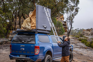 A MAN CLOSING THE ROOFTOP TENT FLINDERS FROM ARB FIXED ON A FORD RANGER BLEUE