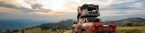 Red Toyota Hilux equipped with a James Baroud grand Raid EVO roof tent and a woman sitting on the tent exit.