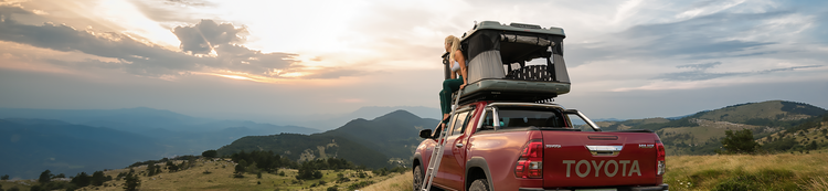 Red Toyota Hilux equipped with a James Baroud grand Raid EVO roof tent and a woman sitting on the tent exit.