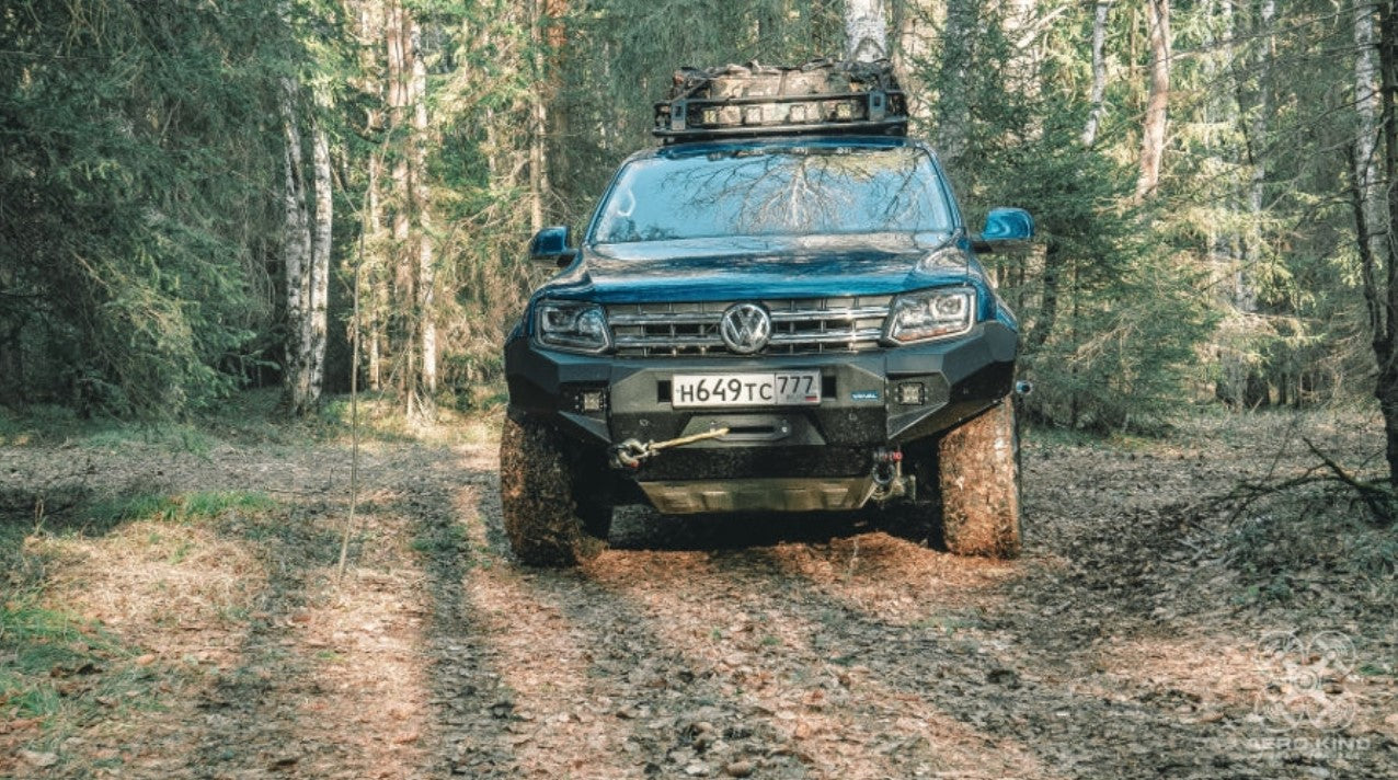 Front view of a blue AMAROK with Rival bumper in a fir forest