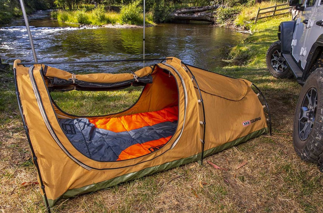 Ground tent on the grass in front of a river with an orange comforter inside