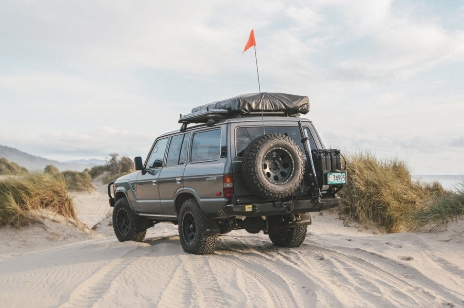 toyota 4x4 in the sand with a black roof tent
